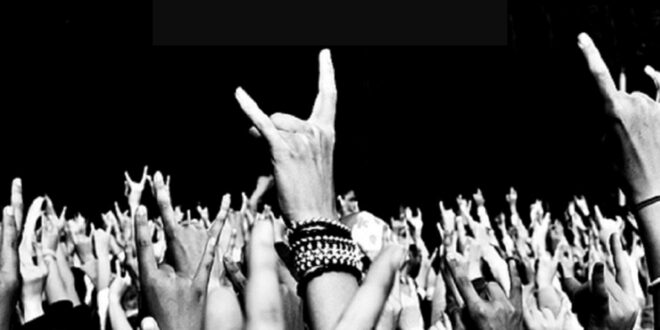 Pra Cego Ver: Foto de várias mãos erguidas fazendo gestos de rock and roll
