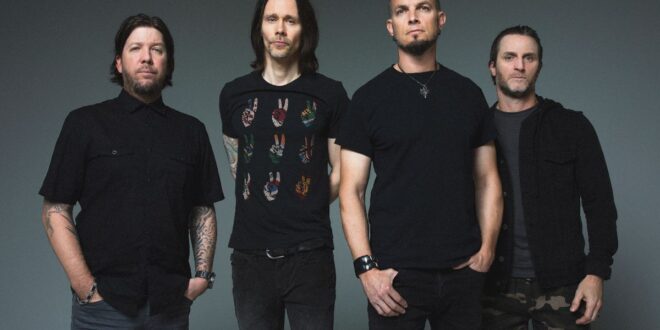Pra Cego Ver: Foto colorida mostra os integrantes da banda Alter Bridge. Todos estão de camisetas pretas e em pé