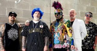 Pra Cego Ver: Foto colorida mostra os integrantes da banda. Eles estão utilizando roupas coloridas e estão em pé do lado um do outro.